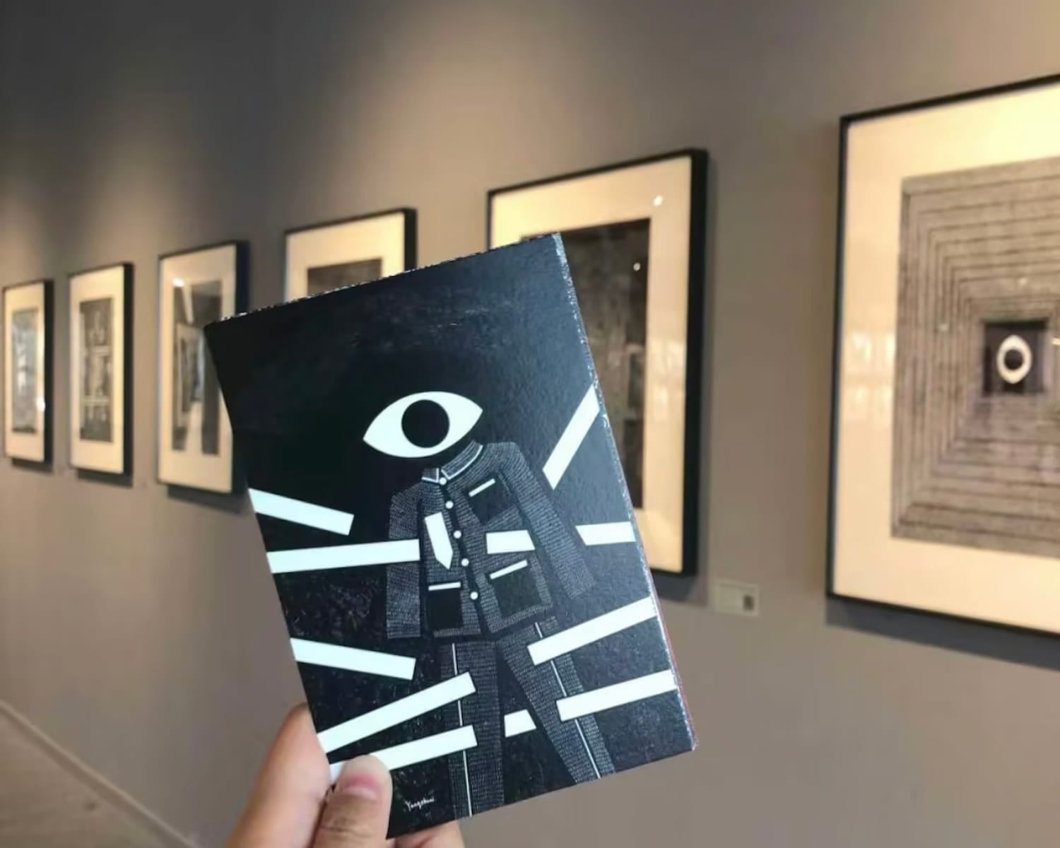 A hand holding an artwork inside a softly lit gallery